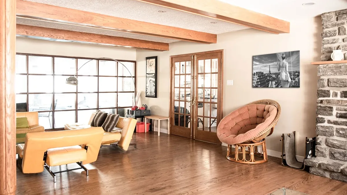 A spacious room with a high ceiling, featuring a large window, a fireplace, and a collection of furniture, including a table, chairs, and a couch, arranged in a living room setting.