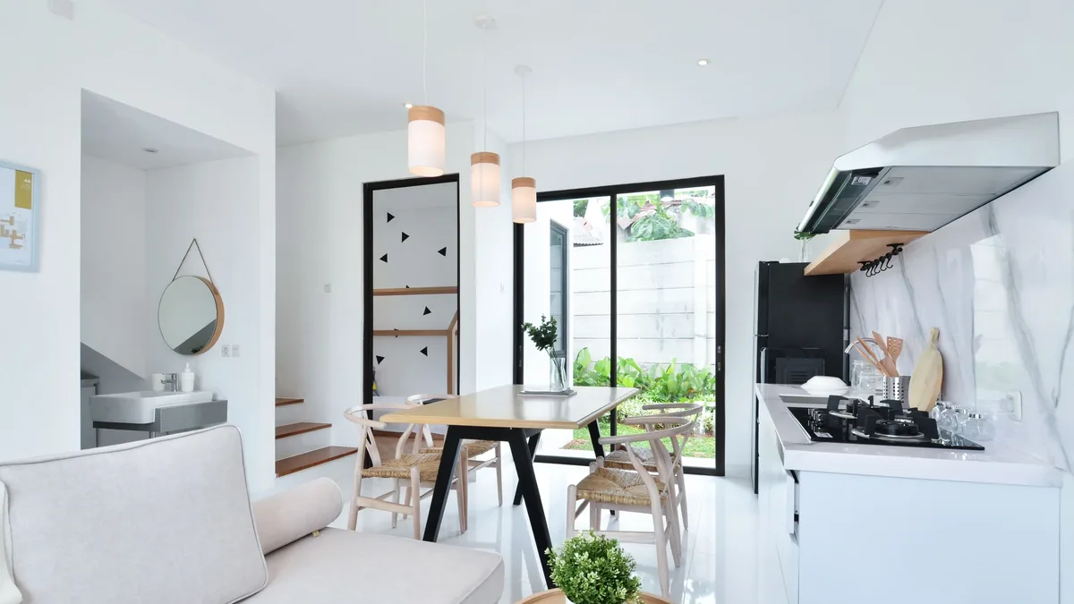 A modern, minimalist living room and kitchen area with a dining table, couch, and kitchen island.